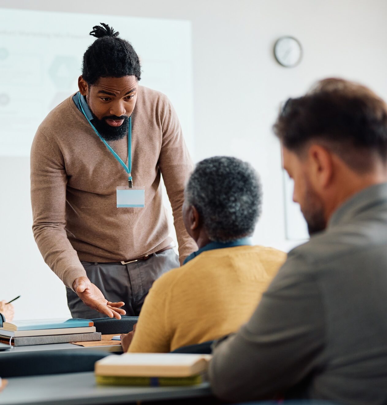 Black teacher talking to senior man during adult education training class in lecture hall.